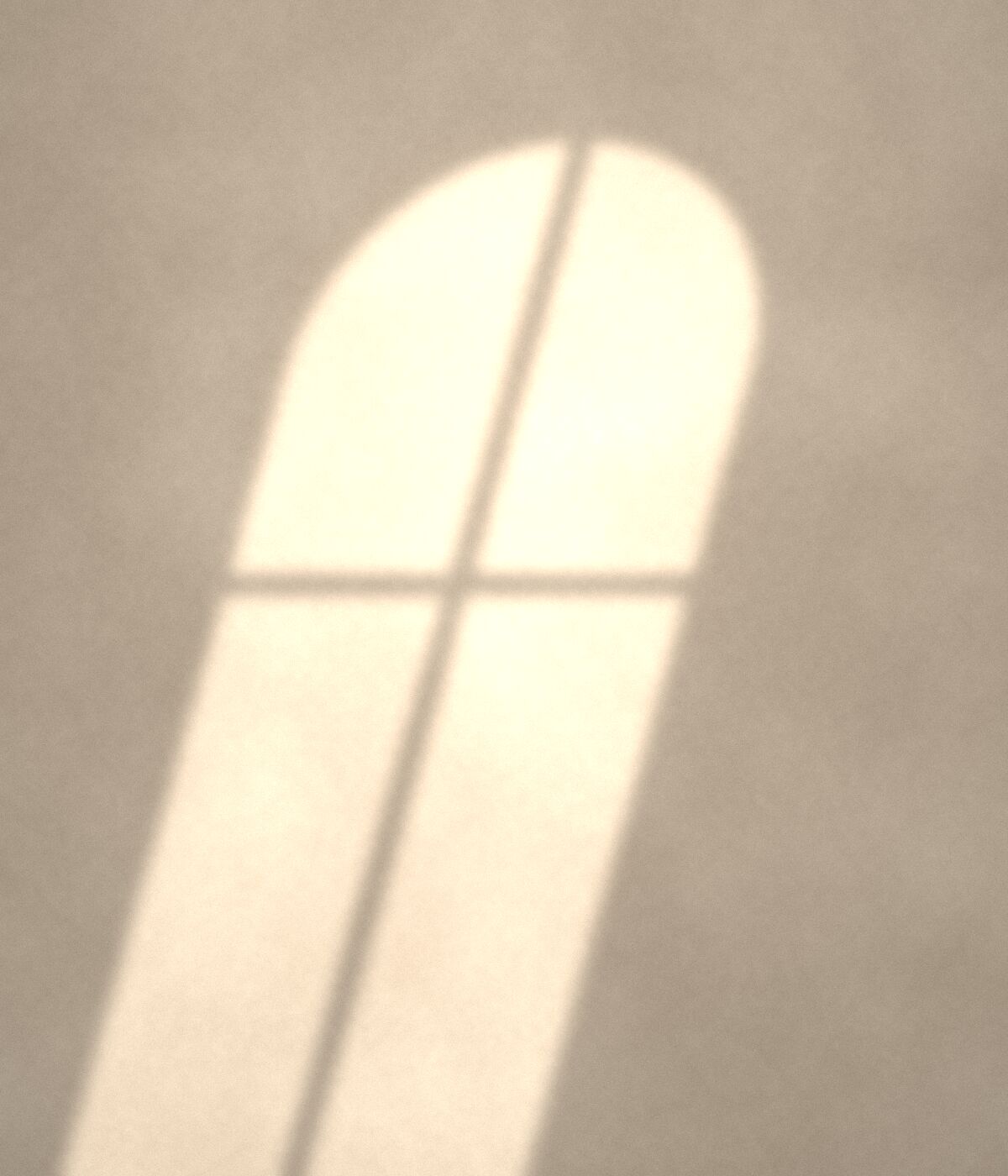 Afternoon sun through an arched window on a plaster wall